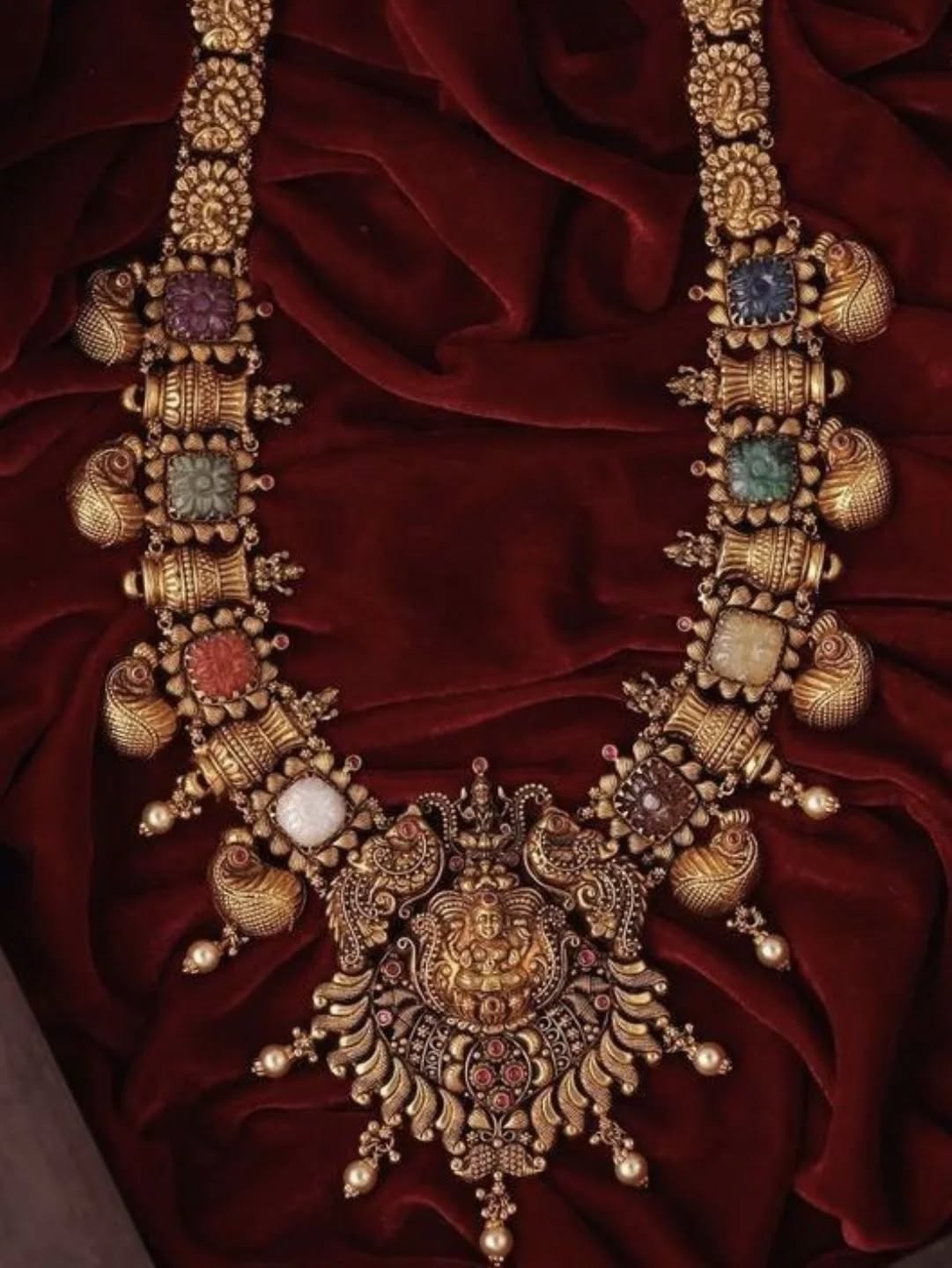 Ornate gold necklace with colorful stones on a red fabric background