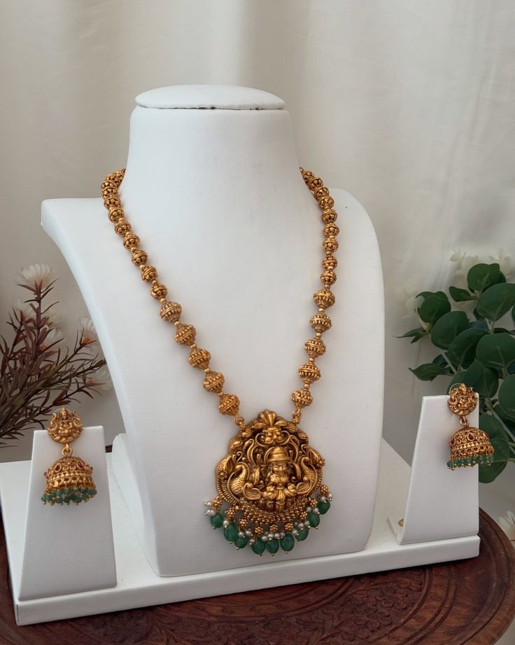 Gold necklace with green beads on a white stand, accompanied by matching earrings.