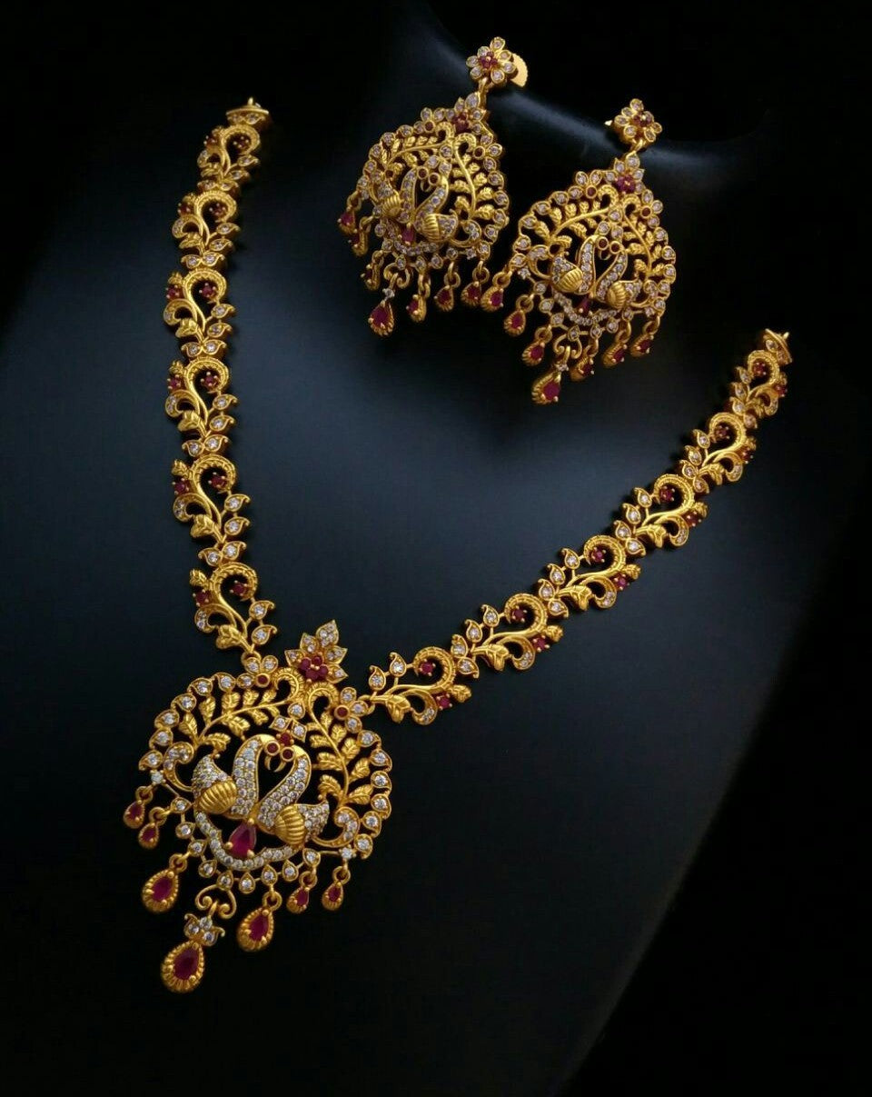 Gold necklace and earrings with red gemstones on a dark background