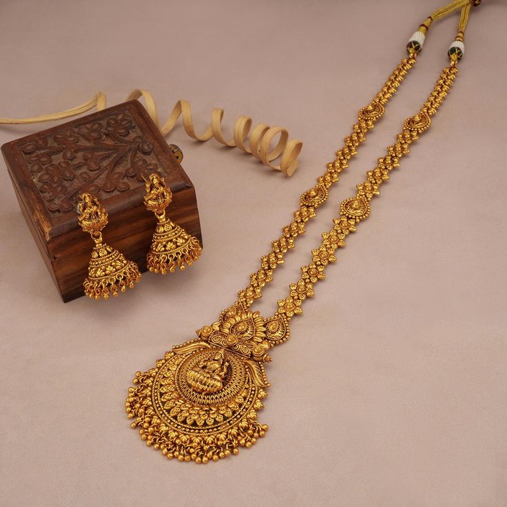 Gold necklace and earrings with a wooden box on a beige background