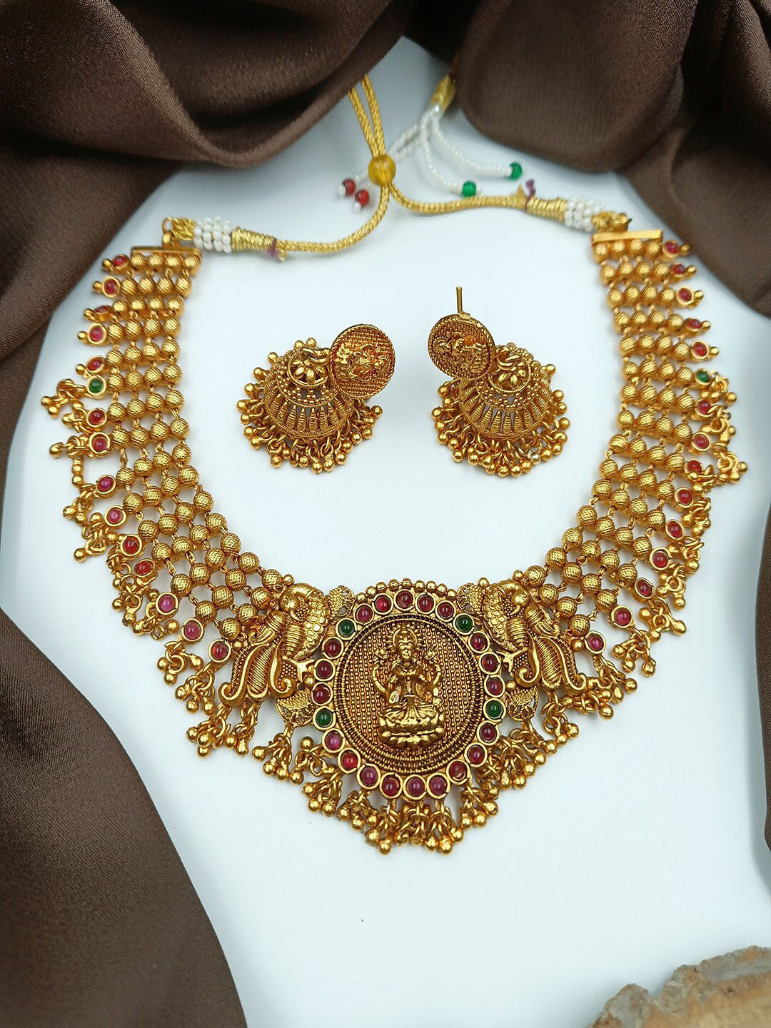 Gold necklace and earrings set on a white and brown fabric background