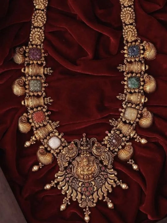 Ornate gold necklace with colorful stones on a red fabric background