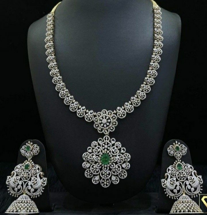 Silver necklace and earrings set on a black mannequin with green gemstones.