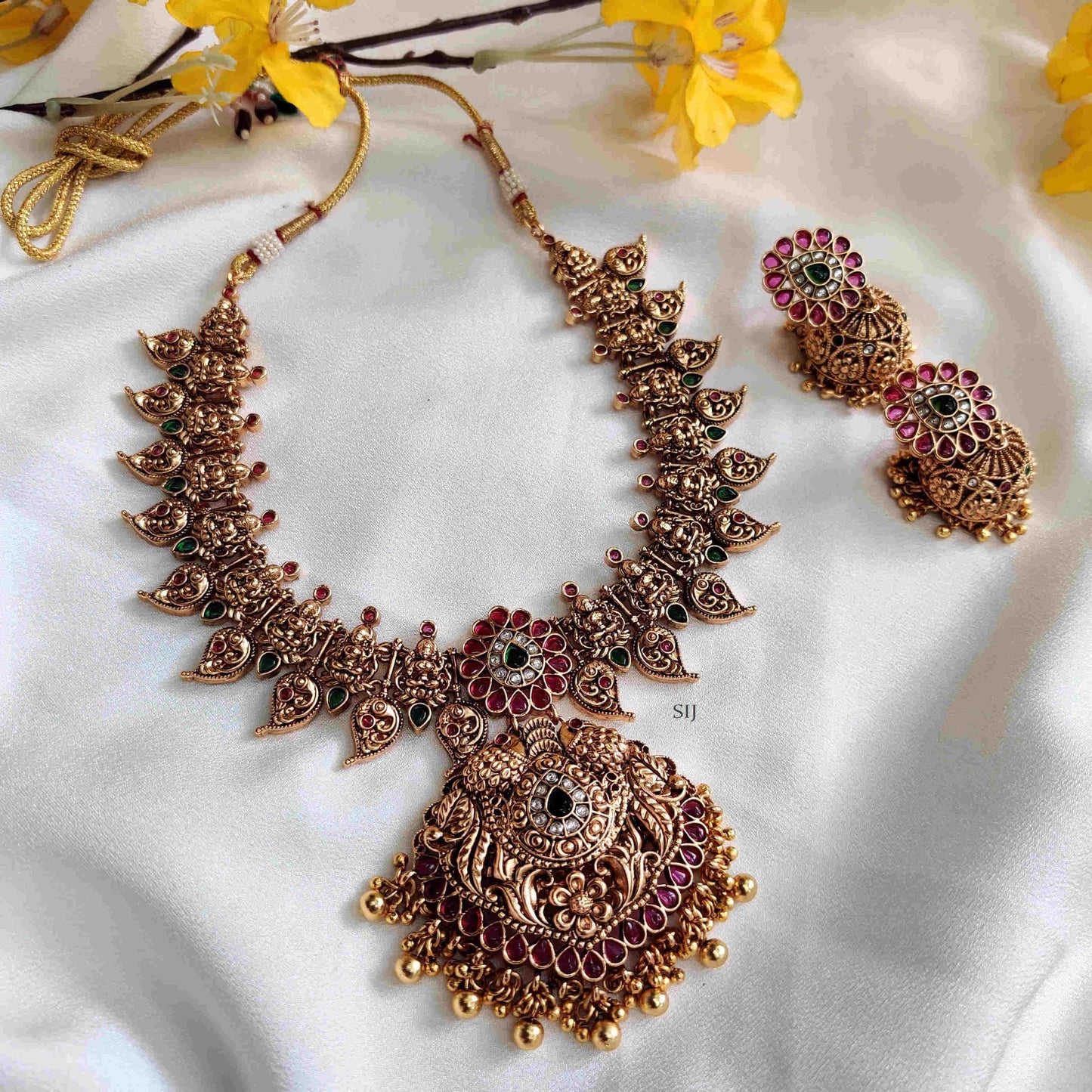 Ornate gold necklace with red and green accents on a white fabric background