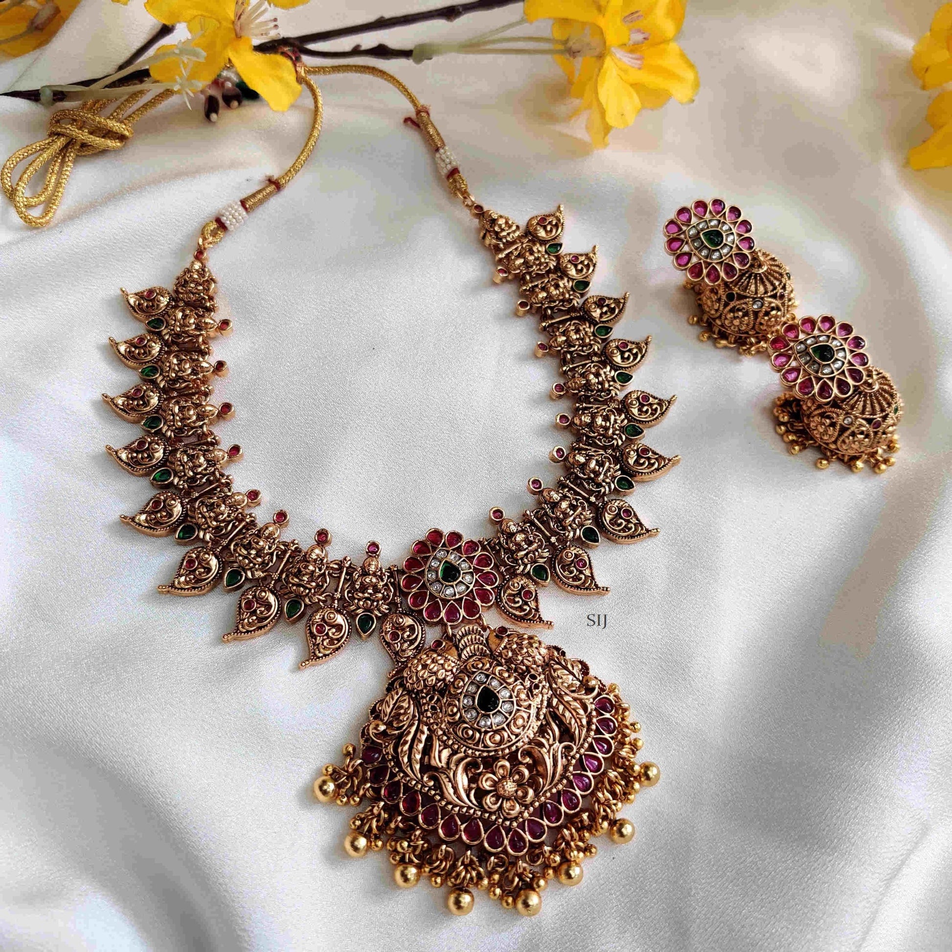Ornate gold necklace with red and green accents on a white fabric background