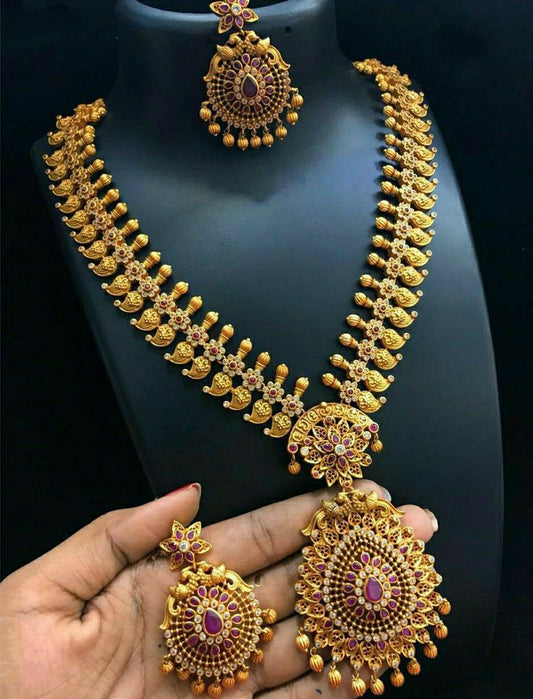 Gold necklace and earrings on a mannequin and hand against a black background