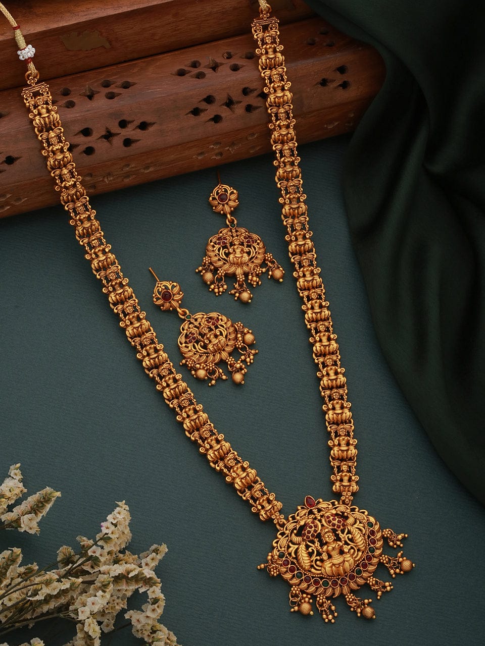 Gold necklace and earrings on a dark surface with a wooden block in the background