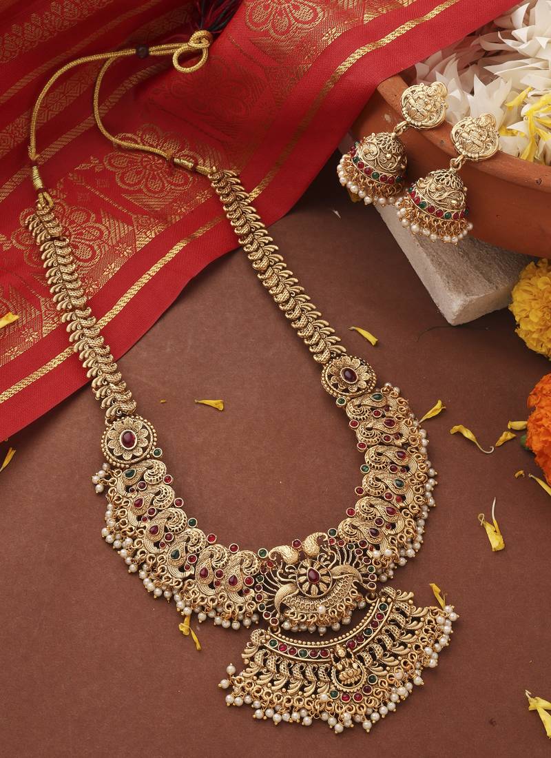Ornate gold necklace with red stones on a brown surface with decorative elements.