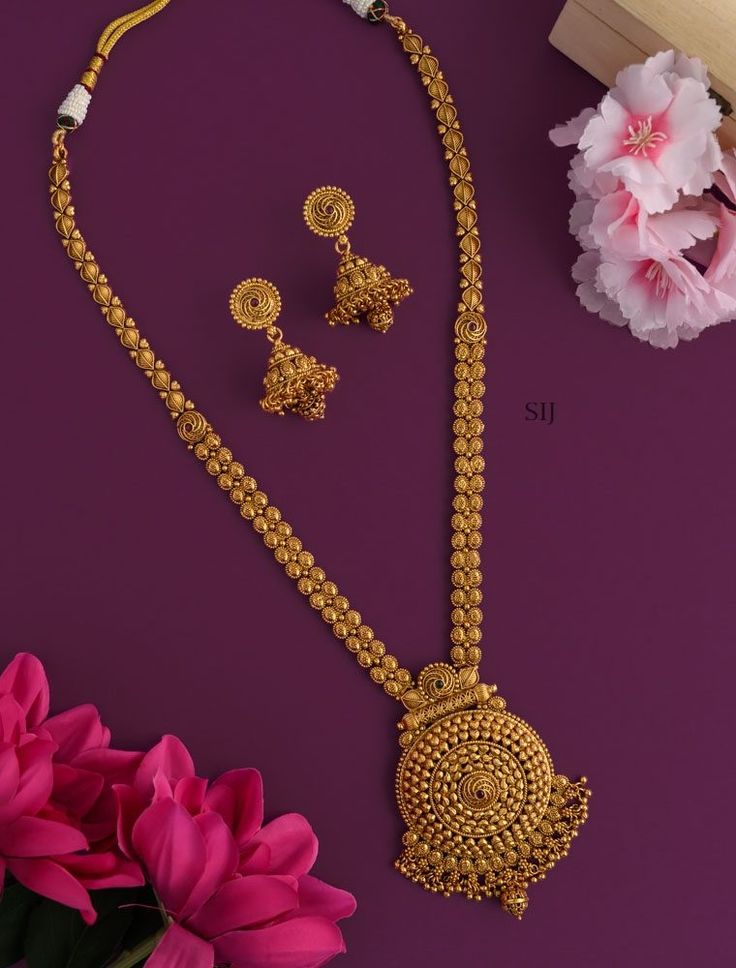 Gold necklace and earrings set on a purple background with pink flowers.