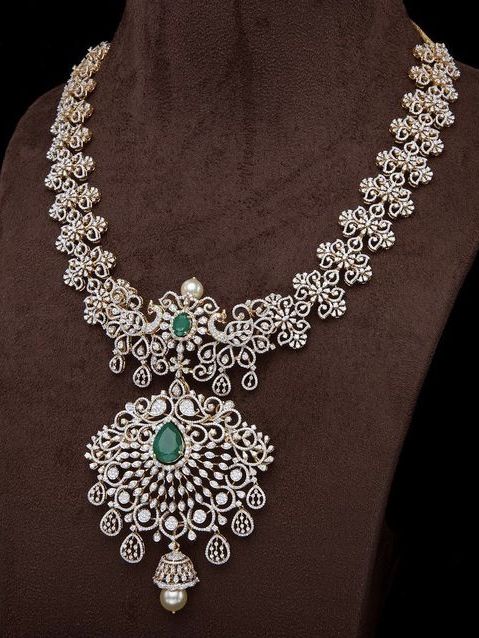 Ornate silver necklace with green gemstones on a brown fabric background